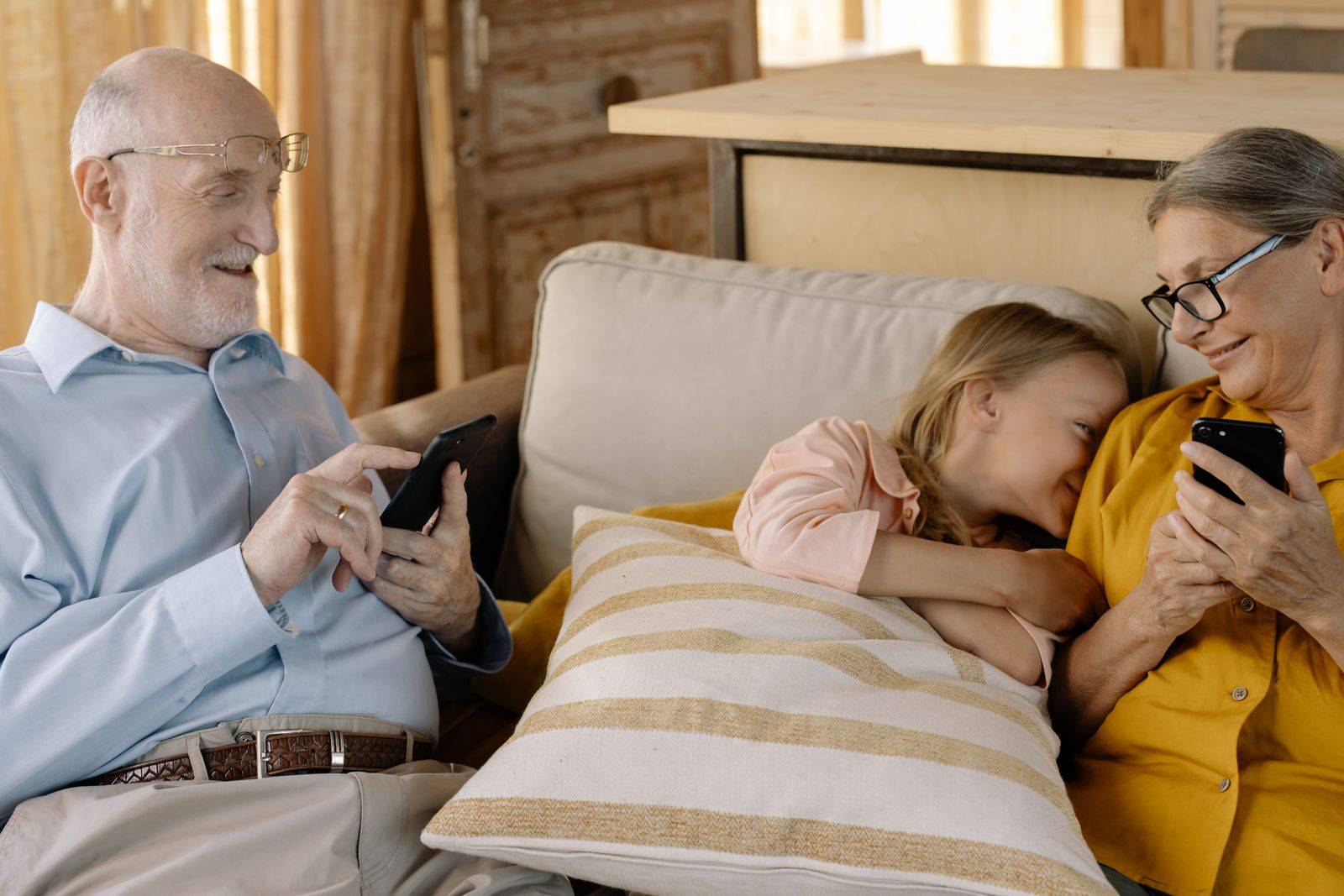 Des grands-parents et leur petite-fille installés sur un canapé, chacun avec un smartphone.