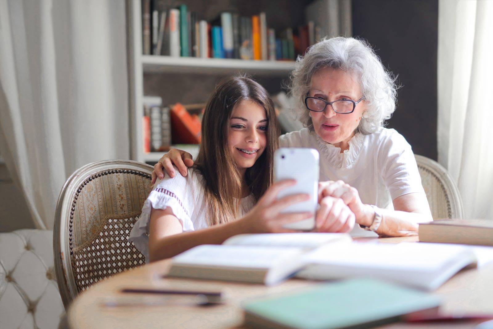 Une jeune femme montre quelque chose sur son smartphone à sa grand-mère, qui sourit.